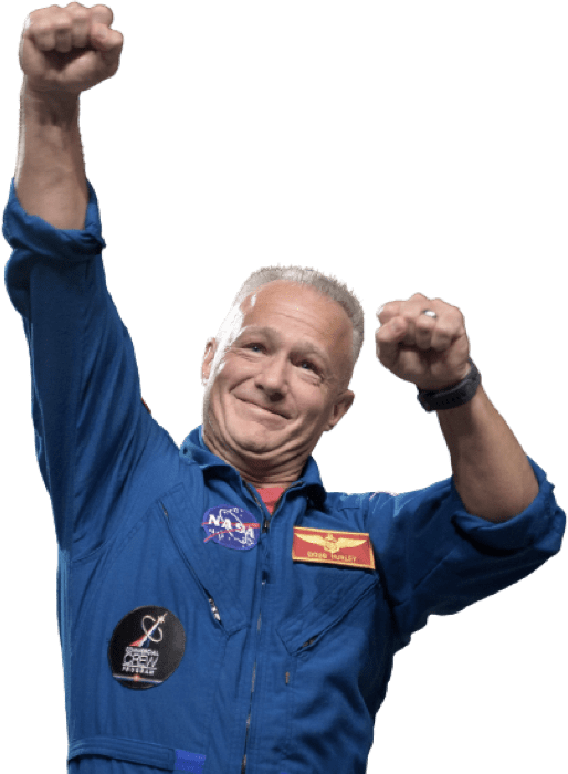 An individual in a blue NASA jumpsuit with patches, raising both arms with clenched fists in a celebratory gesture.