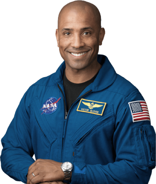 A person wearing a blue NASA astronaut suit with a NASA logo, an American flag patch, and a name tag reading 'Victor Glover'.